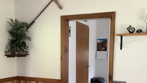 A wooden room with a door, a black mat, a shelf with decorative items, and a wall-mounted plant.