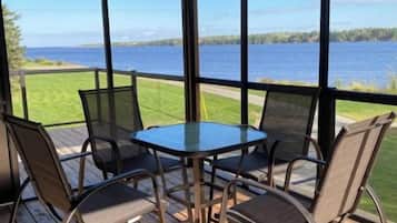 Een overdekt terras met een tafel en stoelen, met uitzicht op een waterpartij.