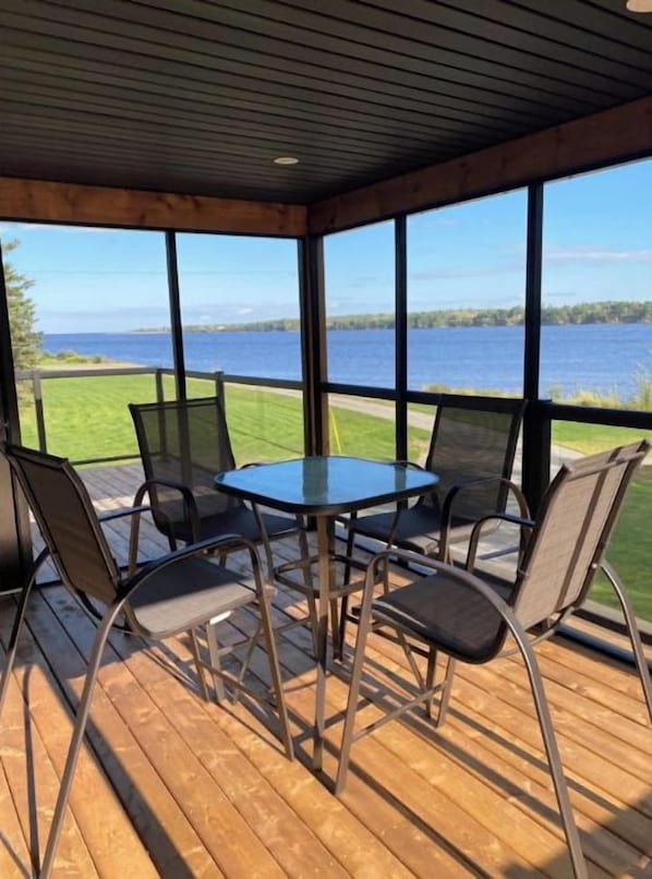 A covered outdoor seating area with a table and chairs, overlooking a body of water.