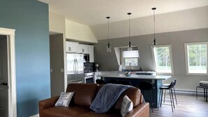 Uma cozinha moderna com eletrodomésticos de aço inoxidável, uma sala de jantar com banquetas de bar e uma sala de estar aconchegante com um sofá de couro marrom.