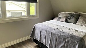 Quarto com cama, travesseiros e janela com cortina escura.