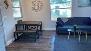 A living room with a sofa, a coffee table, a dining table, and a wall art piece. - Serenity Bungalow Near Armature Works & Riverwalk (Tampa)
