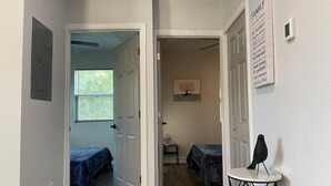 A hallway with two bedrooms, each with a bed and a window. There is a small table with a black object on it. - Serenity Bungalow Near Armature Works & Riverwalk (Tampa)