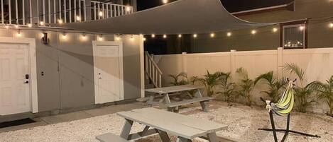Un espace extérieur aménagé en terrasse, avec des tables de pique-nique, des guirlandes lumineuses et un hamac.