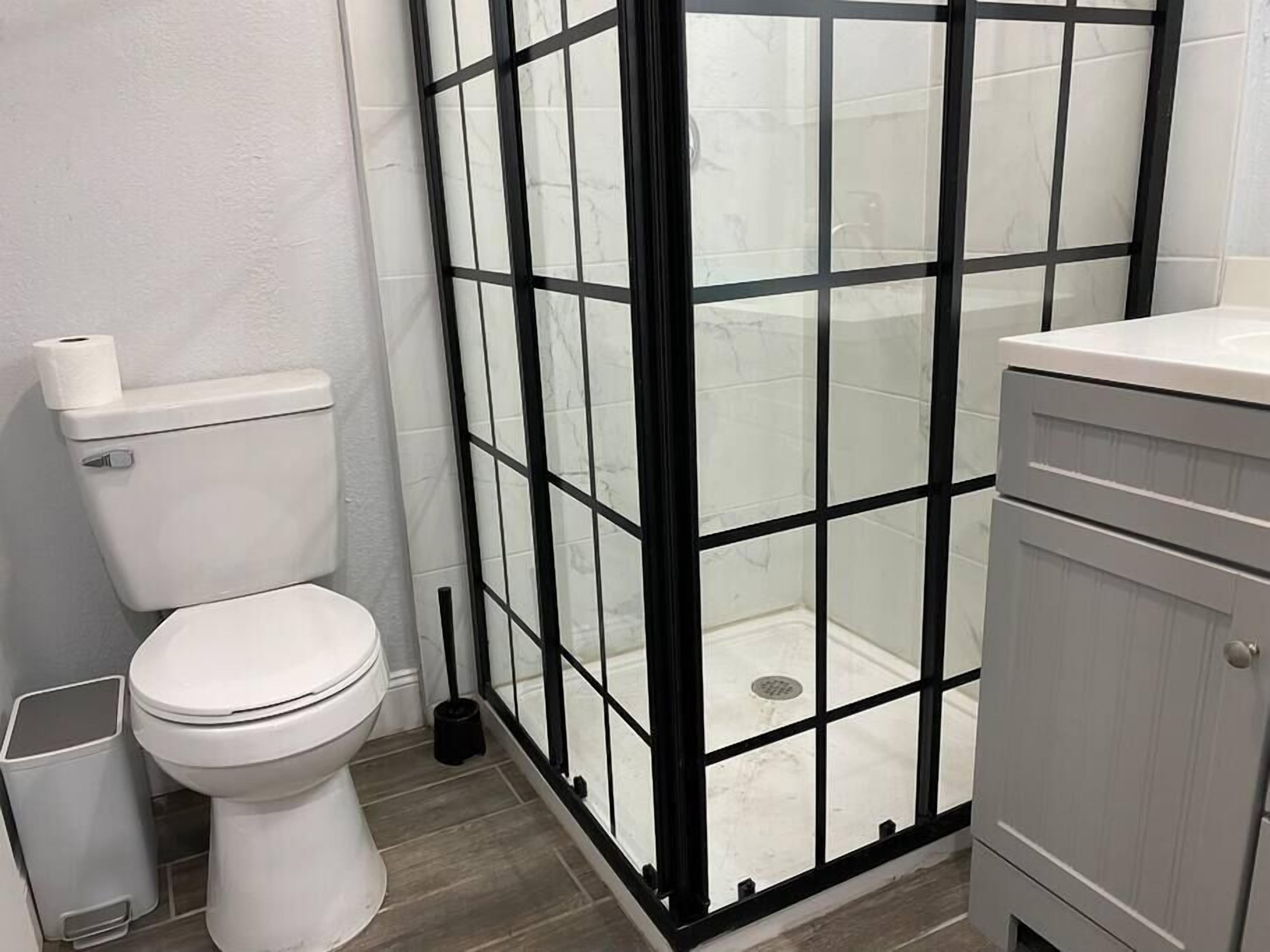 A bathroom with a white toilet, a glass shower enclosure, and a grey cabinet.