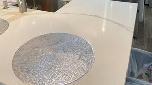 A modern kitchen with grey cabinets, stainless steel appliances, a white countertop, and a unique textured sink basin.