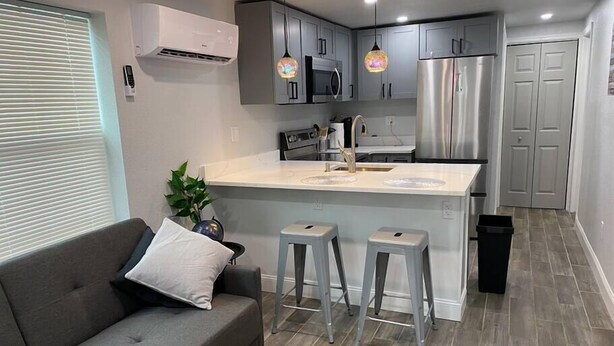 A modern kitchen with grey cabinets, stainless steel appliances, and a central island with stools.