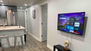 A modern kitchen with a central island, stainless steel appliances, and a flat-screen TV mounted on the wall displaying various streaming services.