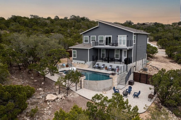 A two-story house with a pool, outdoor seating, and a view of the surrounding forest.