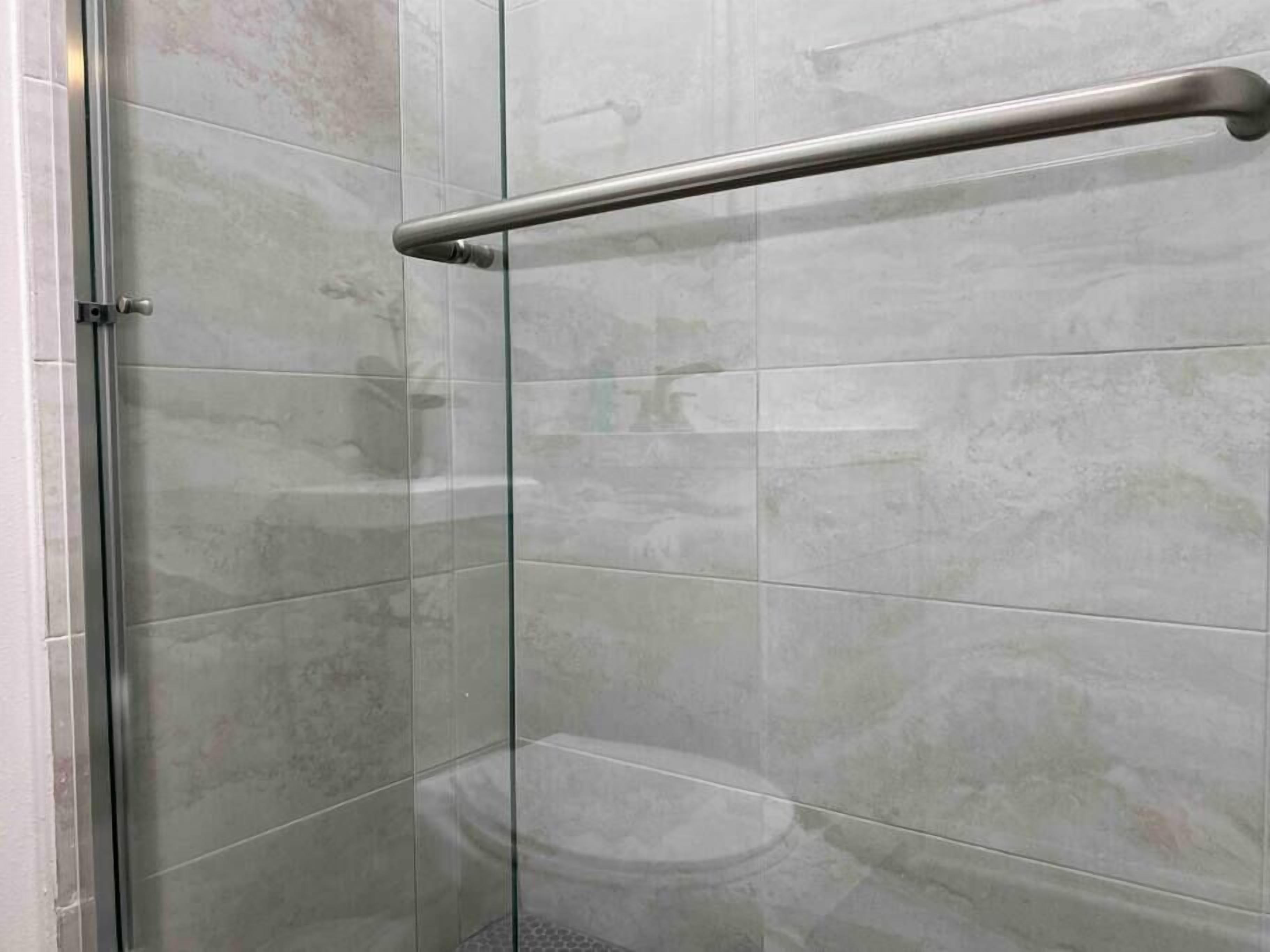 A glass-enclosed shower area with a metal handrail.