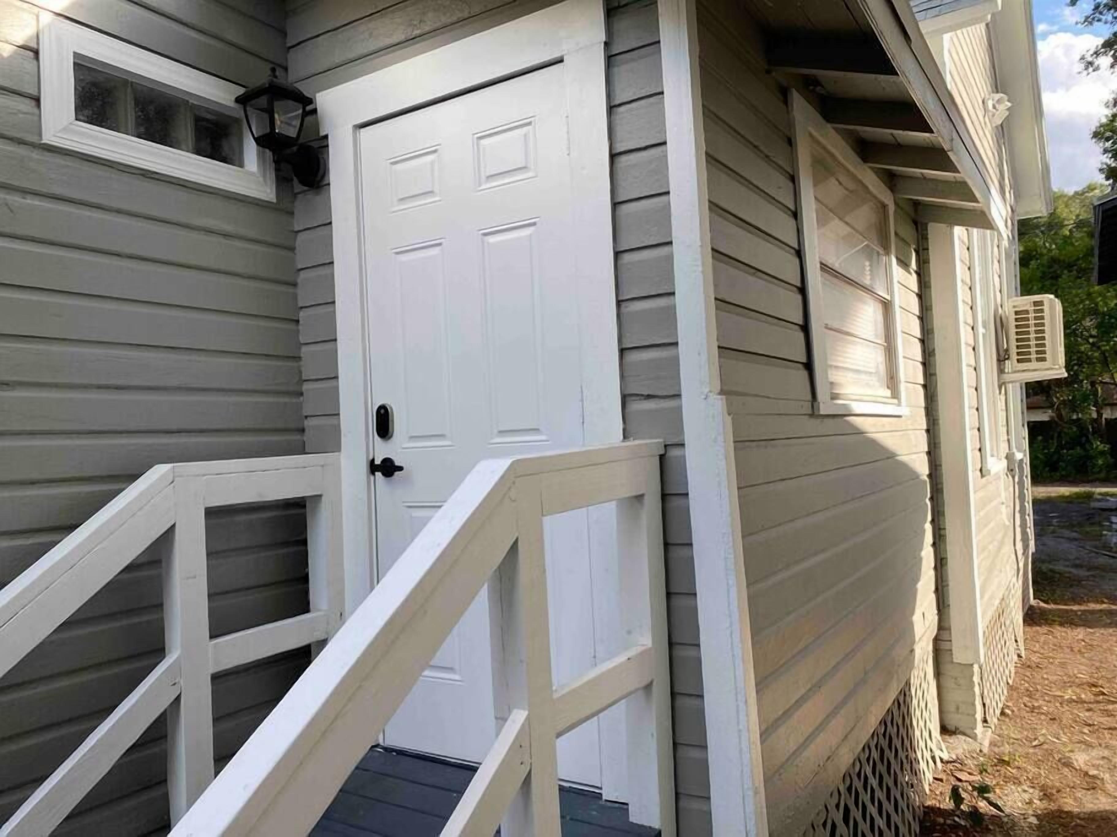 Una casa con una puerta blanca, una ventana pequeña y una barandilla blanca que conduce a la puerta.