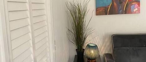 Une pièce avec un canapé gris, une petite table d’appoint noire sur laquelle se trouvent une lampe et une plante, et un tableau abstrait aux couleurs vives accroché au mur.