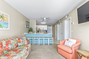 A living room with a sofa, a pink armchair, and a kitchen area with a bar.