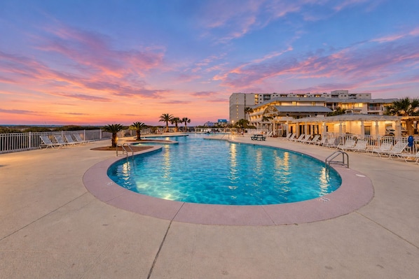 A swimming pool with a curved design, surrounded by lounge chairs and a building with multiple balconies.