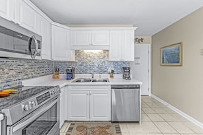 A modern kitchen with white cabinets, a stainless steel dishwasher, and a tiled backsplash.