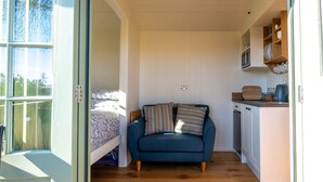 Ein gemütlicher Raum mit Bett, blauem Sofa, einer kleinen Küchenzeile und einem Fenster mit Blick auf Bäume.