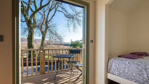 Ein Schlafzimmer mit einem Bett, Blick durch eine Schiebetür auf eine Terrasse mit Tisch und Stühlen sowie einem Holgitter.