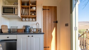 Eine kleine Küche mit Mikrowelle, Wasserkocher und Kaffeemaschine. Eine Holztür führt zu einer Außenterrasse.
