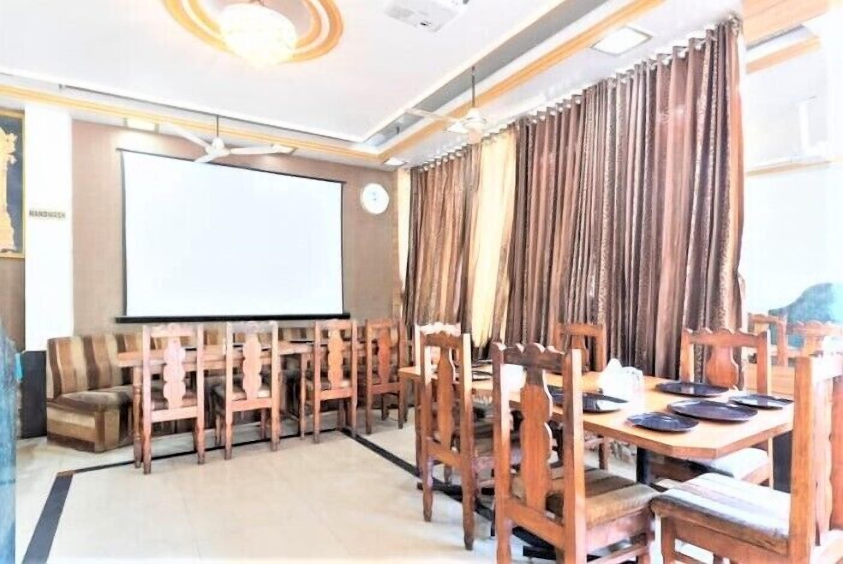Un salón de conferencias con una pantalla grande, sillas de madera, una mesa con platos y cortinas.