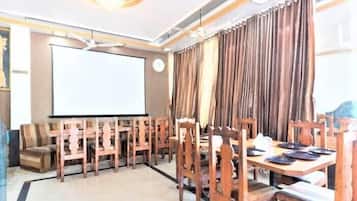Un salón de conferencias con una pantalla grande, sillas de madera, una mesa con platos y cortinas.