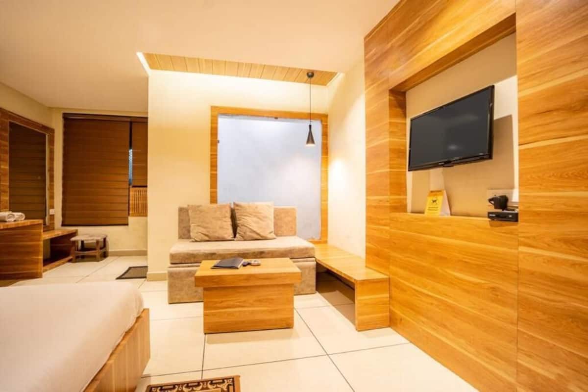 A modern hotel room with a sofa, a bed, a TV mounted on the wall, and a wooden accent wall.