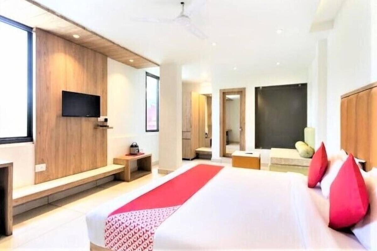 A modern hotel room with a large bed, a flat-screen TV, a wooden accent wall, and a red runner.