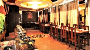 A restaurant with a long counter, multiple tables, and chairs. - Hotel Pachmarhi (Pipariya)