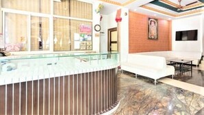 A reception area with a glass counter, white sofa, and a TV mounted on the wall. - Hotel Pachmarhi (Pipariya)