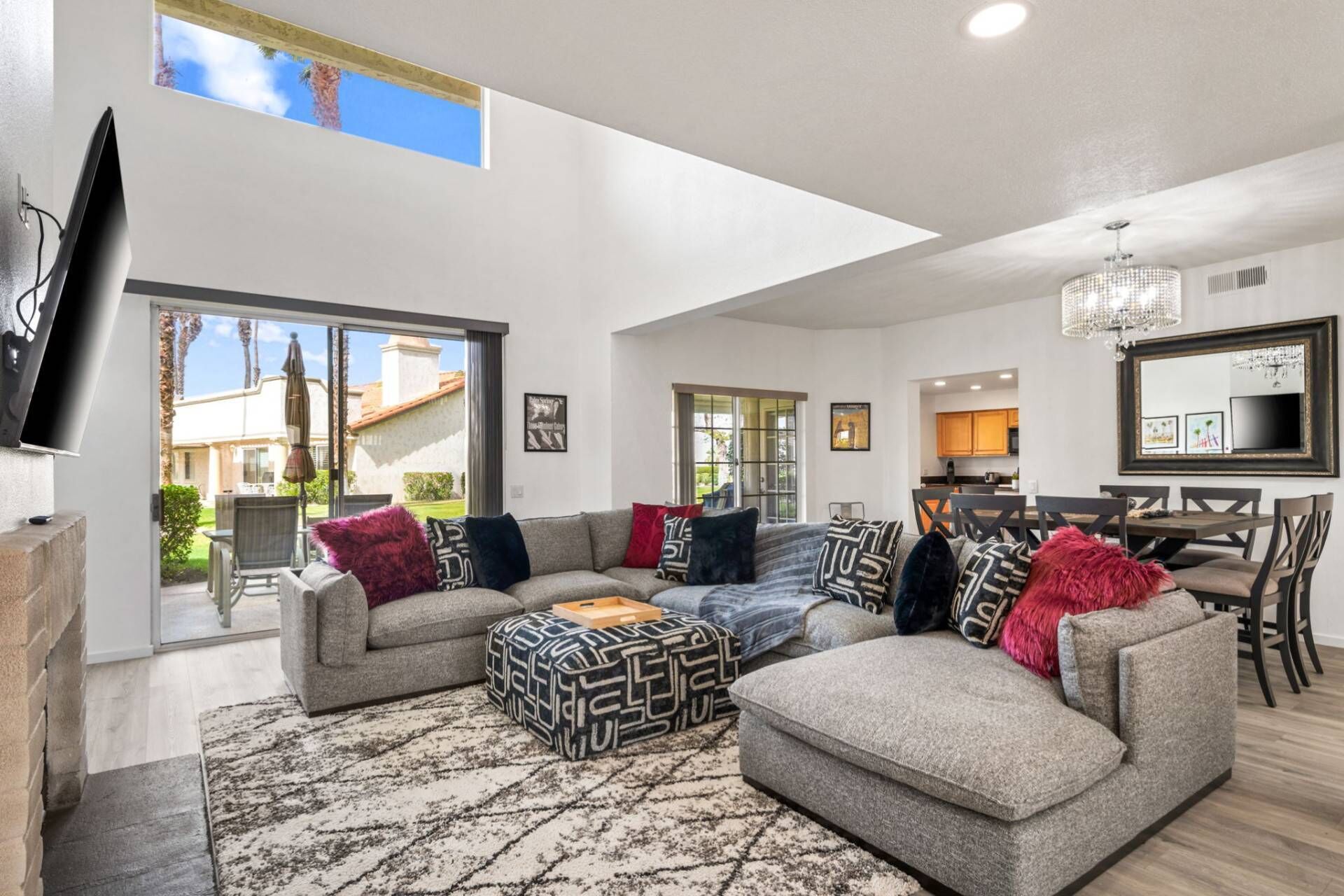 A spacious living room with a large sectional sofa, a flat-screen TV mounted on the wall, and a dining area with a chandelier.