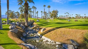 A golf course with a stream, palm trees, and clear skies. - Near Coachella | Desert Falls Home | Steps to Pool, Spa, & Fun! Mountain Views Out Your Window! (Palm Desert)