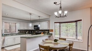 A modern kitchen with white cabinets, a central island, and a dining area with wooden chairs. - Chetola Resort: Robin 1 - Lower Level Unit near downtown Blowing Rock (Blowing Rock)