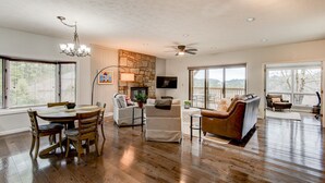 A spacious living room with hardwood floors, a stone fireplace, a chandelier, and a dining area with a table and chairs. - Chetola Resort: Robin 1 - Lower Level Unit near downtown Blowing Rock (Blowing Rock)