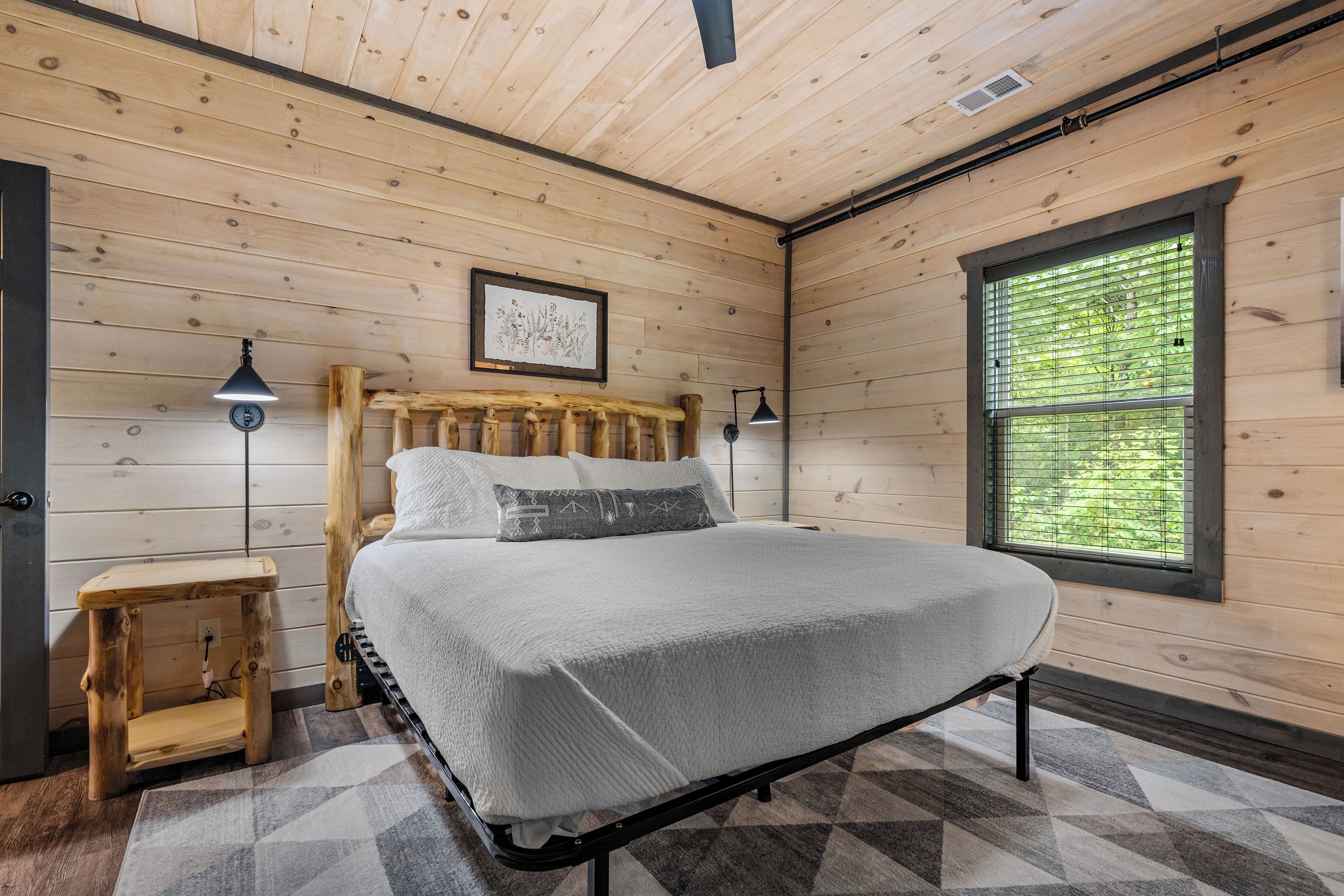 Une chambre à coucher aux murs lambrissés, avec un lit, des lampes de chevet, un petit tabouret en bois et une fenêtre équipée de stores.