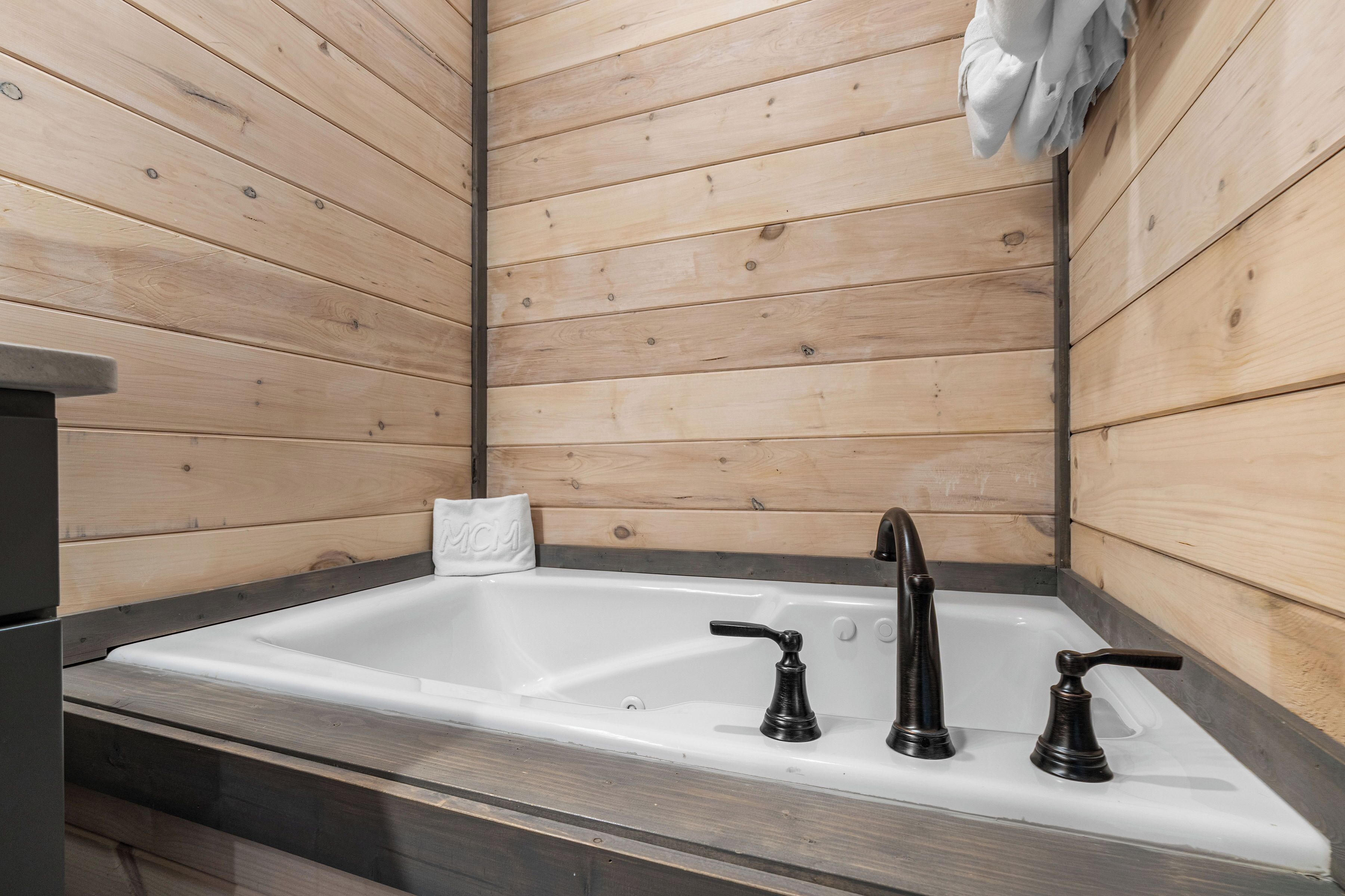 A bathroom with a wooden wall, a white sink, and three black faucets.