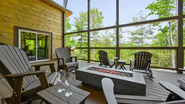 En träveranda med Adirondack-stolar, en eldstad och ett glasbord med vinglas.