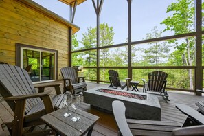 Een houten terras met Adirondack-stoelen, een vuurkuil en een glazen tafel met wijnglazen.