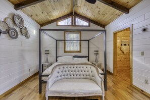 Classic four-poster bed with tufted headboard, sloped ceiling, and white wood paneling.