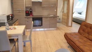 Una cucina compatta con elettrodomestici moderni, un'area pranzo con tavolo e sedie, e un angolo salotto accogliente con un divano marrone.