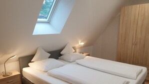 Una camera da letto con un lucernario, un letto con lenzuola bianche, un comodino con una lampada e un armadio.