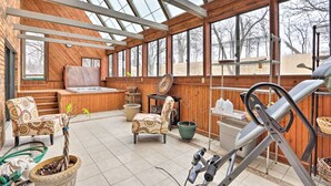 Un espacio interior amplio con suelo de madera, un jacuzzi y un ventanal que ofrece vistas a árboles.