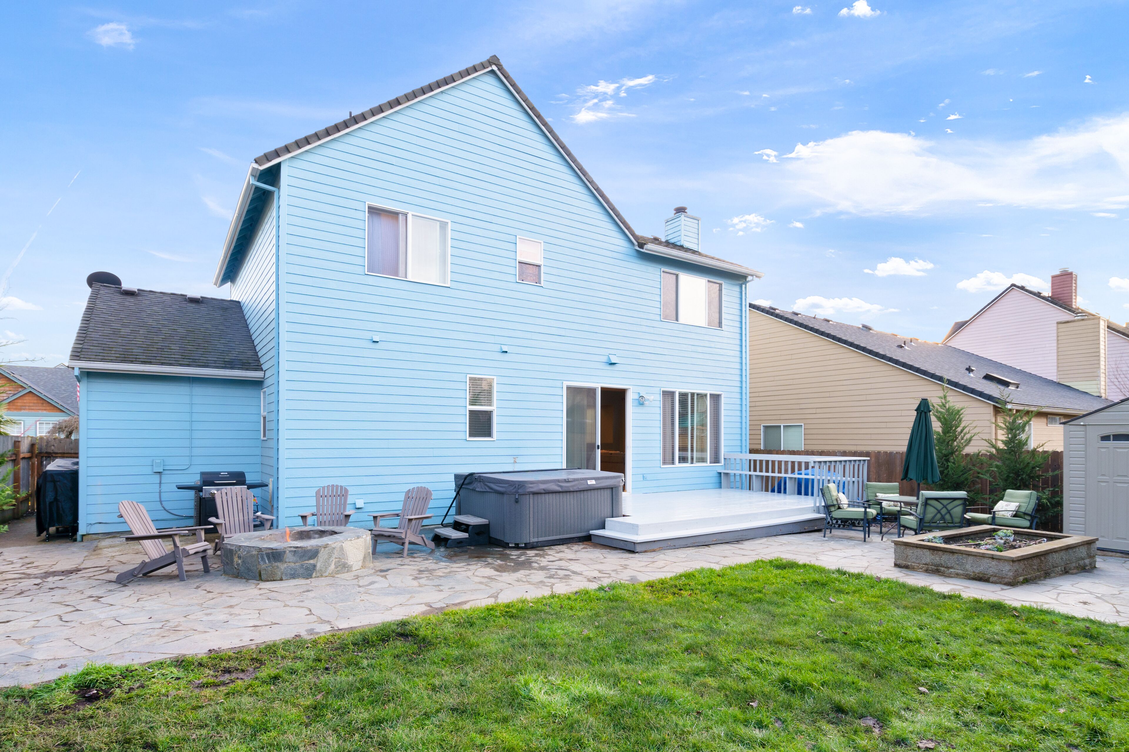 Een huis met twee verdiepingen, met een blauwe gevel, een terras met tuinmeubilair en een jacuzzi.