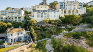 A coastal hotel with multiple buildings, including a prominent 'VERNON COURT' sign, situated on a hillside with lush greenery and rocky terrain. - De'nada, Vernon Court -  an apartment that sleeps 2 guests  in 1 bedroom (Torquay)