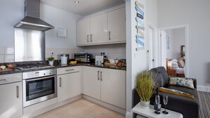 A modern kitchen with stainless steel appliances, white cabinetry, and a dining area with a sofa and a small table. - Sea-la-vie, Astor House -  an apartment that sleeps 4 guests  in 1 bedroom (Torquay)