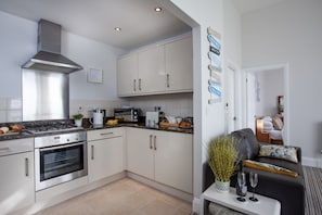 A modern kitchen with stainless steel appliances, white cabinetry, and a dining area with a sofa and a small table.