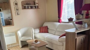 Ett kompakt bostadsutrymme med en soffa, ett litet bord, en liten köksdel och ett fönster med gardiner.
