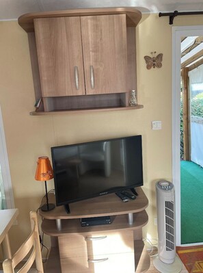 A compact living space with a TV on a wooden stand, a small table, and a cabinet above.