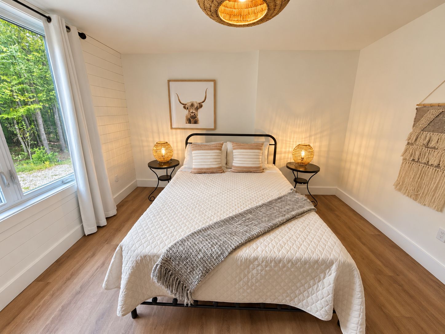 Une chambre à coucher avec un lit, des lampes de chevet, un tableau encadré au mur et une fenêtre avec des rideaux.