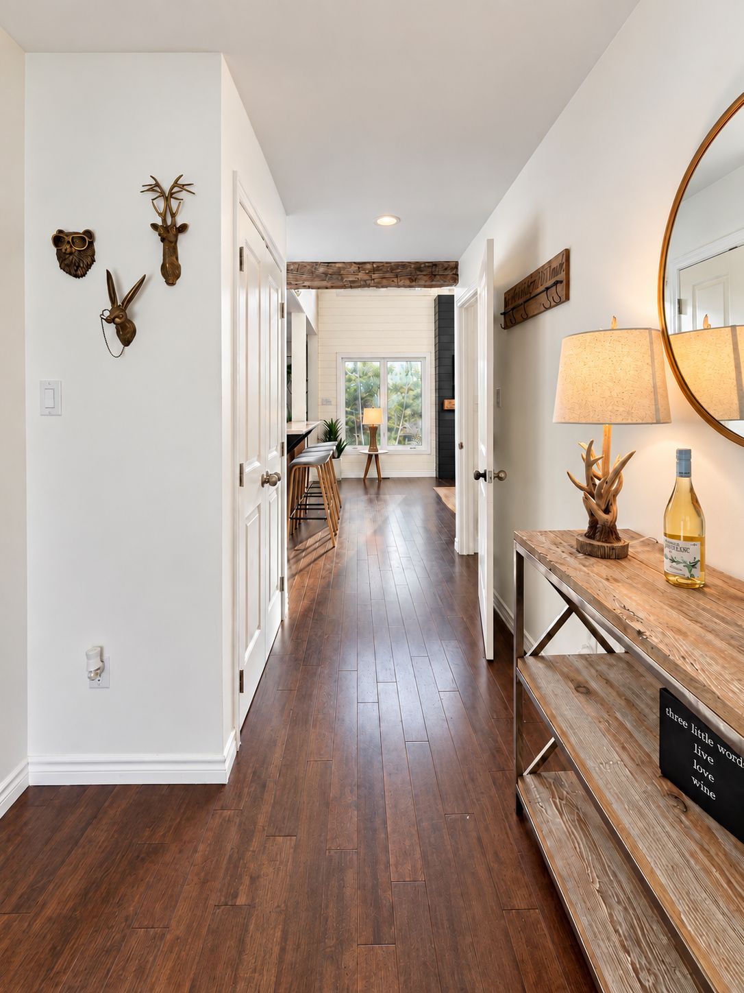 A hallway with wooden flooring, a bench, a lamp, and wall-mounted deer antlers.