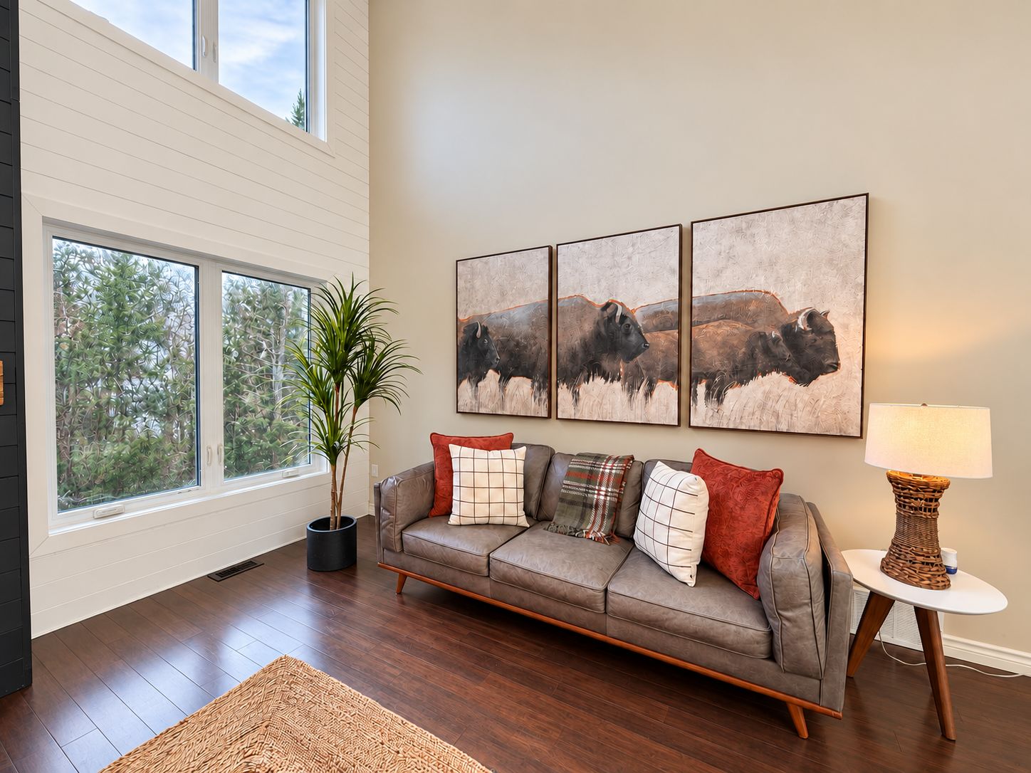 A living room with a sofa, a lamp, and a painting of bison.