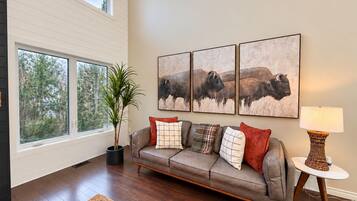 A living room with a sofa, a lamp, and a painting of bison.